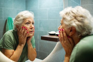 Senior woman examining face in mirror