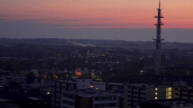 Distant skyline at twilight. Video pans across a city skyline under a fading purple sky as day turns to night, with lights beginning to glow.