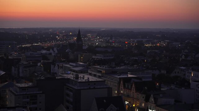 Fiery sunset above city. Video captures a vibrant orange-red sunset fading over city rooftops, lights shimmering as night approaches.