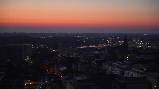 City glowing at dusk. Video pans over a city with glowing streetlights and illuminated buildings under a deep orange evening sky.