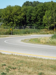 A sharp curve in an asphalt road. The road has white lane markings and a solid yellow line in the foreground.
