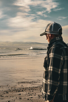 Man overlooking the ocean, wearing a cap