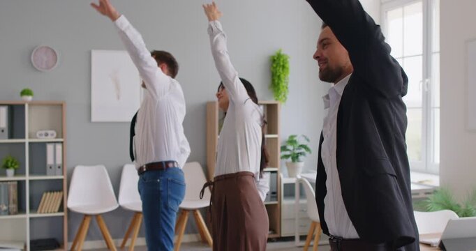 Coworkers in an office raise arms overhead, stretching during a quick exercise break. Warmup supports fitness and posture while improving mood. Quick team stretch routine for office energy.
