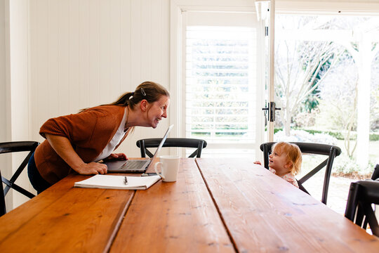 Woman leaning over wooden table smiling to toddler daughter on the opposite end