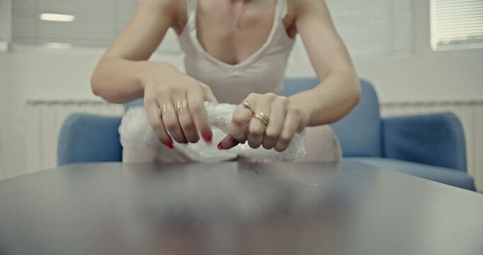 Enjoy the satisfying sounds of a woman popping bubble wrap on a table. This video captures the tactile and auditory delight of a simple, stress-relieving activity, perfect for an ASMR experience.