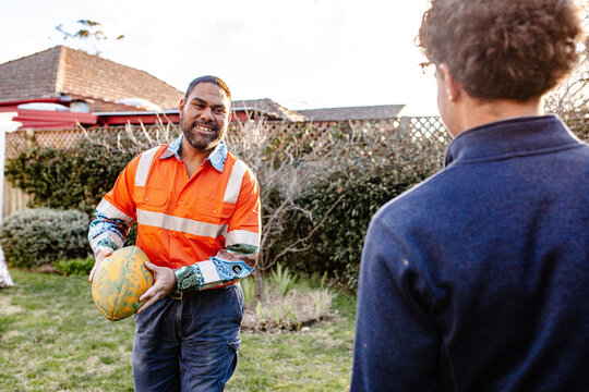 Father in high vis clothing playing with ruby ball with teenage son in the garden