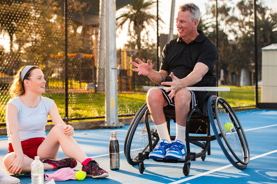 Man in wheelchair and woman sitting on tennis court talking after practice - Powered by Adobe