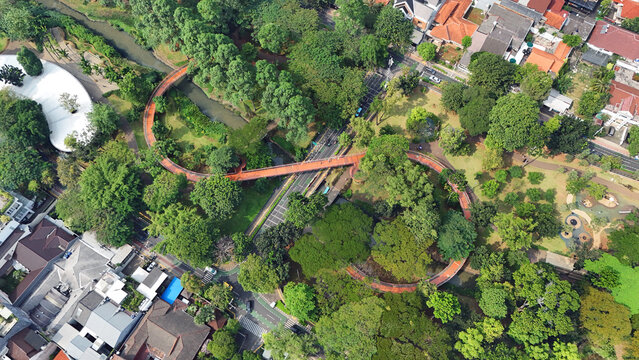 Aerial view of a unique infinity bridge curving through lush greenery and over a tranquil river, blending urban architecture with nature's serenity, Solo, Central Java, Indonesia.