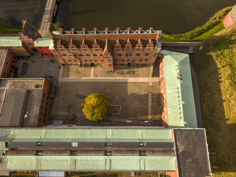 Aerial view of the Malmo Castle's weathered brick and green copper roofs, contrasting with the golden tree in the courtyard, Malmo, Scania County, Sweden.