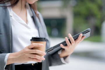 Close up hand of businesswoman standing holding coffee while using tablet outdoors city, digital nomad, business woman or manager touching tablet for working, modern technology, digital device.
