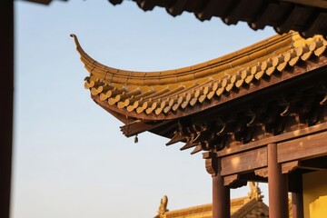 Traditional Chinese architectural roof with upturned eaves and golden tiles against a clear sky