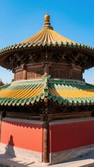 Fototapeta premium Traditional Chinese pavilion with ornate yellow and green tiled roof and red walls under a clear blue sky