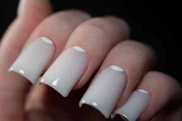 Professional manicure with milky white nails. Feminine hands with trendy nail design, concept of style, fashion, and clean beauty in close-up.