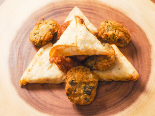 Indian style starter food selection of samosa, bhajis and pakoras on wooden board background. Party sharing finger food variety made from fine products and aromatic spices. Special orient vibe.