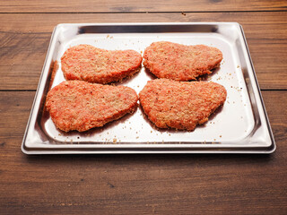 Lamb uncooked steak coated in Arabic Harissa style herbs and spices on stainless metal tray on wooden table. Red minced meat. Fine butcher style burgers ready for cooking.