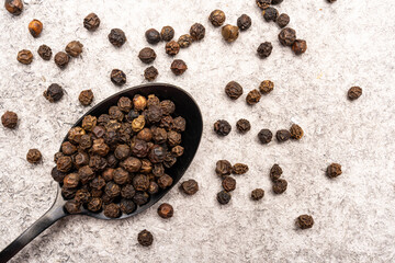 Black peppercorns on white stone table  background