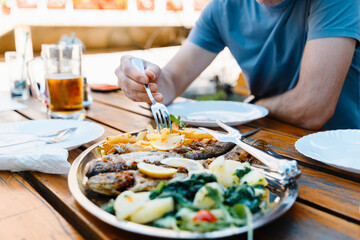 Mediterranean culinary. Istrian grilled fish with potatoes and vegetables served outdoors in Croatian restaurant. People enjoying Grilled Sea Bream with a glass of beer at summer vacation
