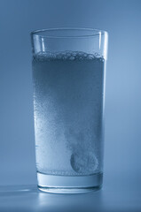 Tablet dissolving in a glass of water on blue background