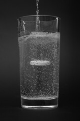 Tablet dissolving in a glass of water on black background