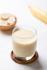 Banana milk in glass with sliced banana and fruit on white background