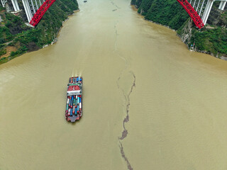 A cargo ship travels on the Yichang Three Gorges river in China under a large bridge, showing the...