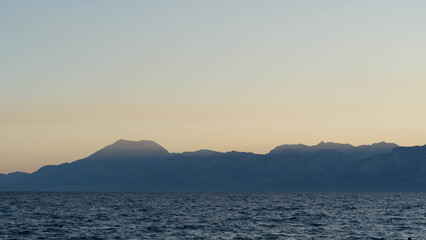 Mountain Silhouette Over Calm Sea During Sunset