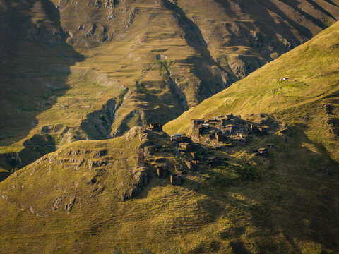 Aerial view of ancient stone buildings clustered on a grassy hilltop, framed by the rugged slopes of the Caucasus mountains, Dartlo, Kakheti, Georgia.