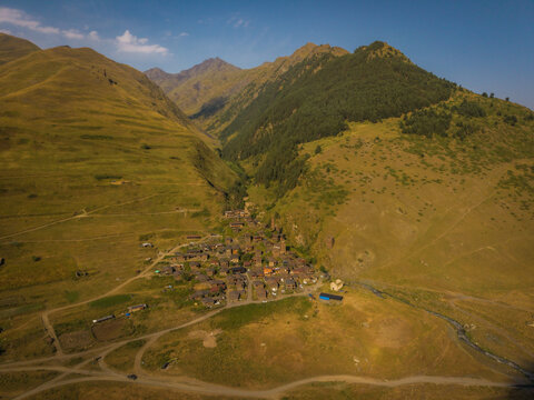 Aerial view of a remote village nestled between rolling hills and rugged mountains, where traditional stone houses cluster along a winding river, Dartlo, Kakheti, Georgia.