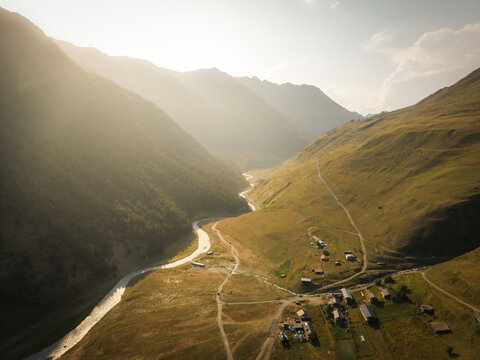 Aerial view of sunlight bathing the rugged, grassy slopes descending into the valley, where a winding river reflects the golden hour near Dartlo, Kakheti, Georgia.