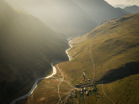 Aerial view of sunlight kissing the rugged peaks, a river snaking through the valley, and the village of Dartlo nestled in the folds of Tusheti, Dartlo, Kakheti, Georgia.