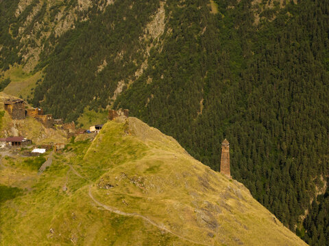 Aerial view of a medieval stone tower rising from a grassy hill, framed by dark green forests and the village of Dartlo, Dartlo, Kakheti, Georgia.