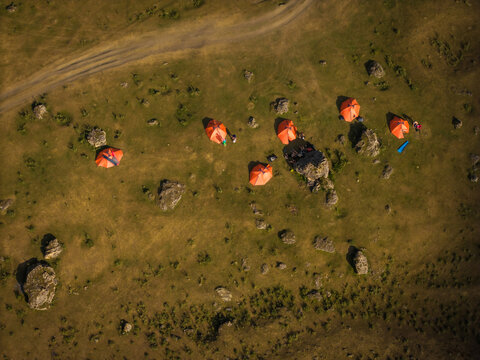 Aerial view of bright orange tents clustered amidst the rugged terrain and scattered rocks of a verdant landscape, Dartlo, Kakheti, Georgia.