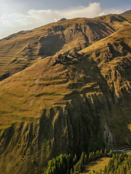 Aerial view of golden, sun-drenched slopes cascading down rugged mountainsides, meeting lush green forests in the valleys below, Dartlo, Kakheti, Georgia.