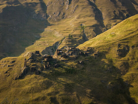 Aerial view of ancient stone buildings nestled between rolling green hills, bathed in warm sunlight and casting long shadows, Dartlo, Kakheti, Georgia.
