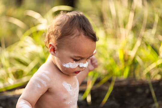 Young First Nations Australian toddler boy painted in ochre in green bushland