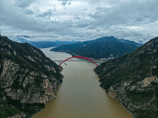 A red bridge spans the Yangtze River through steep green mountains in Yichang, China, under a...