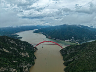 Yichang Three Gorges China landscape shows a red bridge spanning a wide river valley surrounded by...