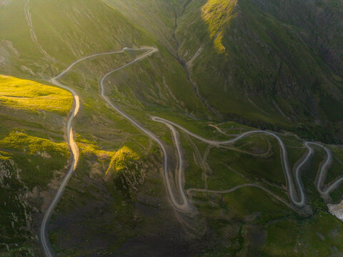Aerial view of winding roads cutting through the verdant, textured mountains, where sunlight paints the slopes in warm gold, contrasting with the cool shadows, Chala, Kakheti, Georgia.