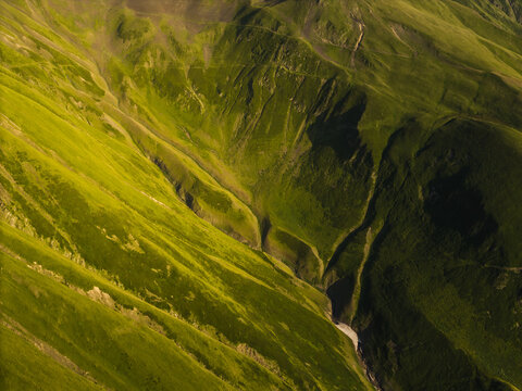 Aerial view of verdant slopes cascading down rugged terrain, a symphony of green hues punctuated by stark shadows, Chala, Kakheti, Georgia.