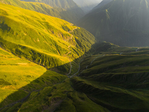 Aerial view of a valley bathed in sunlight, contrasting sharply with the shadowy depths of the Alazani Pass, Chala, Kakheti, Georgia.