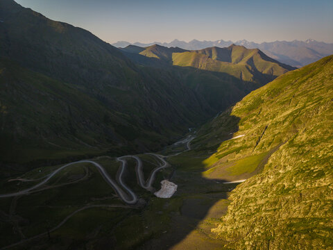 Aerial view of winding road snaking through the rugged Alazani Pass, where light and shadow dance across the steep, verdant slopes, Chala, Kakheti, Georgia.