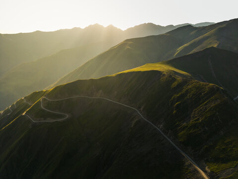 Aerial view of winding roads snaking through sun-kissed, verdant mountain ridges under a golden sky, Alazani pass, Chala, Kakheti, Georgia.