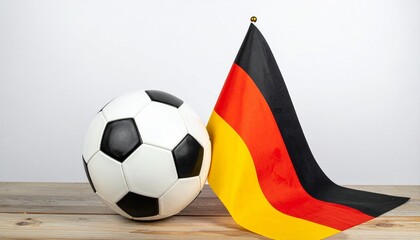 Soccer ball beside small German flag on wooden surface with white background