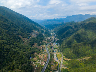 Vast China valley unfolds with green mountains and a winding highway through small villages, showing a natural landscape.