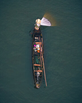 Aerial view of a solitary boat cuts through the still, dark waters, its occupant casting a net, creating a striking contrast of light and shadow, Epe, Lagos, Nigeria.