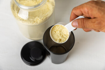 Protein shake with protein powder on a colored background. The powder is mixed with water or milk. A dietary supplement for a balanced diet. Whey protein. Fitness and gym diet nutrition.