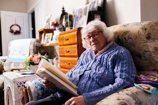 Older Aussie woman sitting on armchair in loungeroom reading a fiction novel