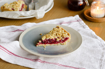 Close up of Italian sbriciolata crumble pie slice with organic plum jam on plate over white towel. Thanksgiving autumn dessert