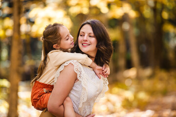 Fototapeta premium Mature mother giving piggyback ride to small daughter on a walk in autumn forest.
