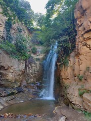 Waterfall among rocky canyon surrounded by green trees, nature travel landscape